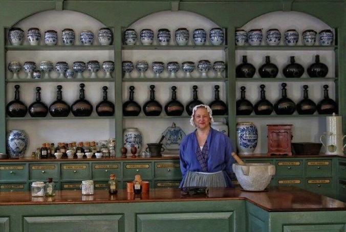 Apothecary Sharon Cotner stands in front of antique drug jar collection in the Pasteur & Galt Apothecary. (Photograph by Fred Blystone; courtesy of Colonial Williamsburg Foundation).